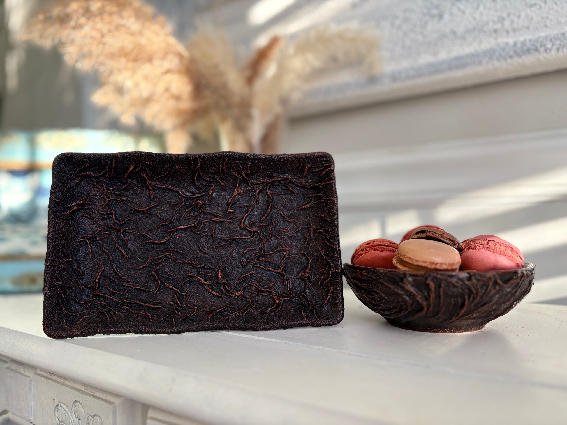 Dark brown textured clutch bag on a white surface with a small bowl of colorful macarons.