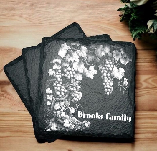 Set of slate coasters with grapevine design and 'Brooks family' text on a wooden surface.